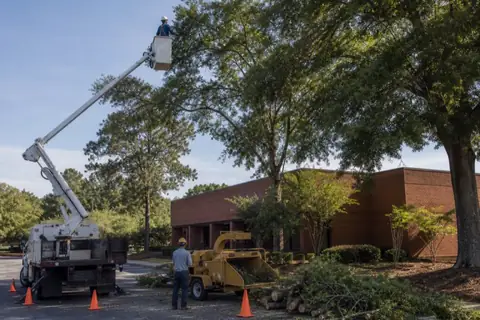 Bucket lift pruning parking-lot trees at a plain brick Macon office property without visible signage